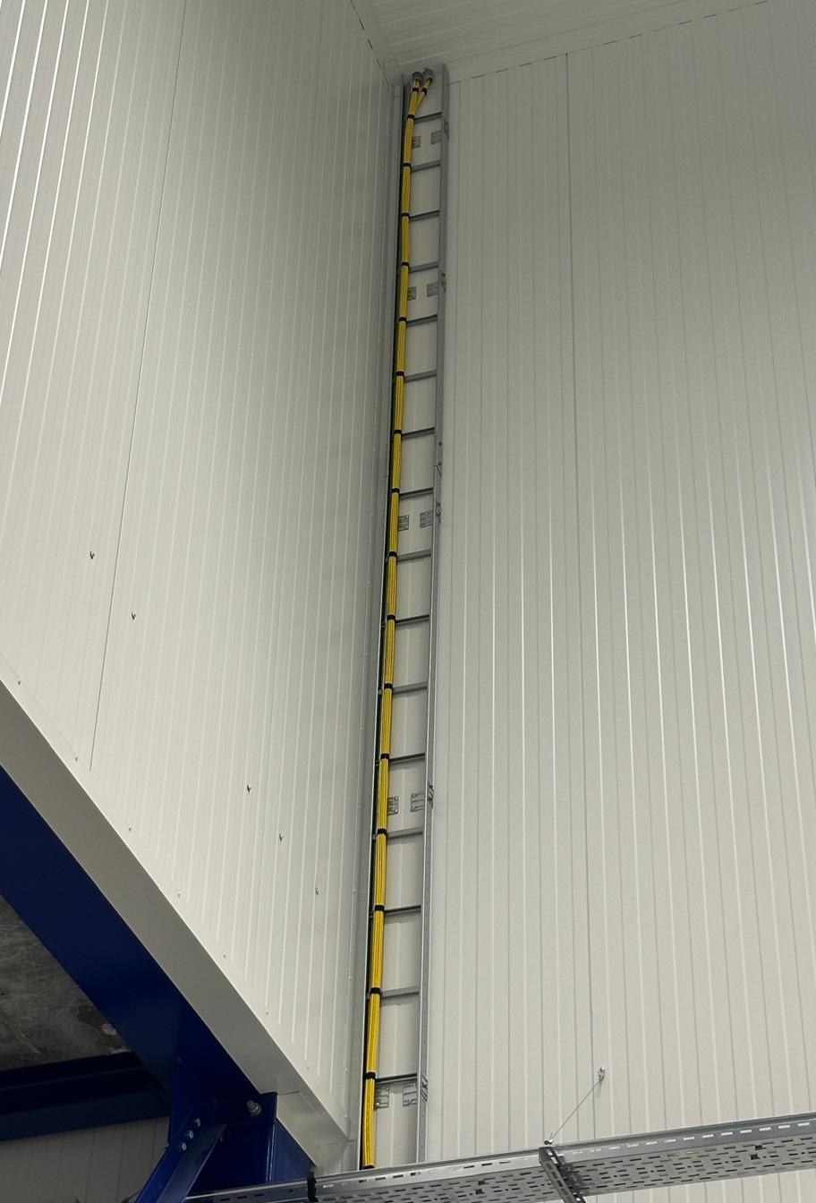 Gele kabelbundel op een hoge kabelladder tegen een sandwichpaneelwand